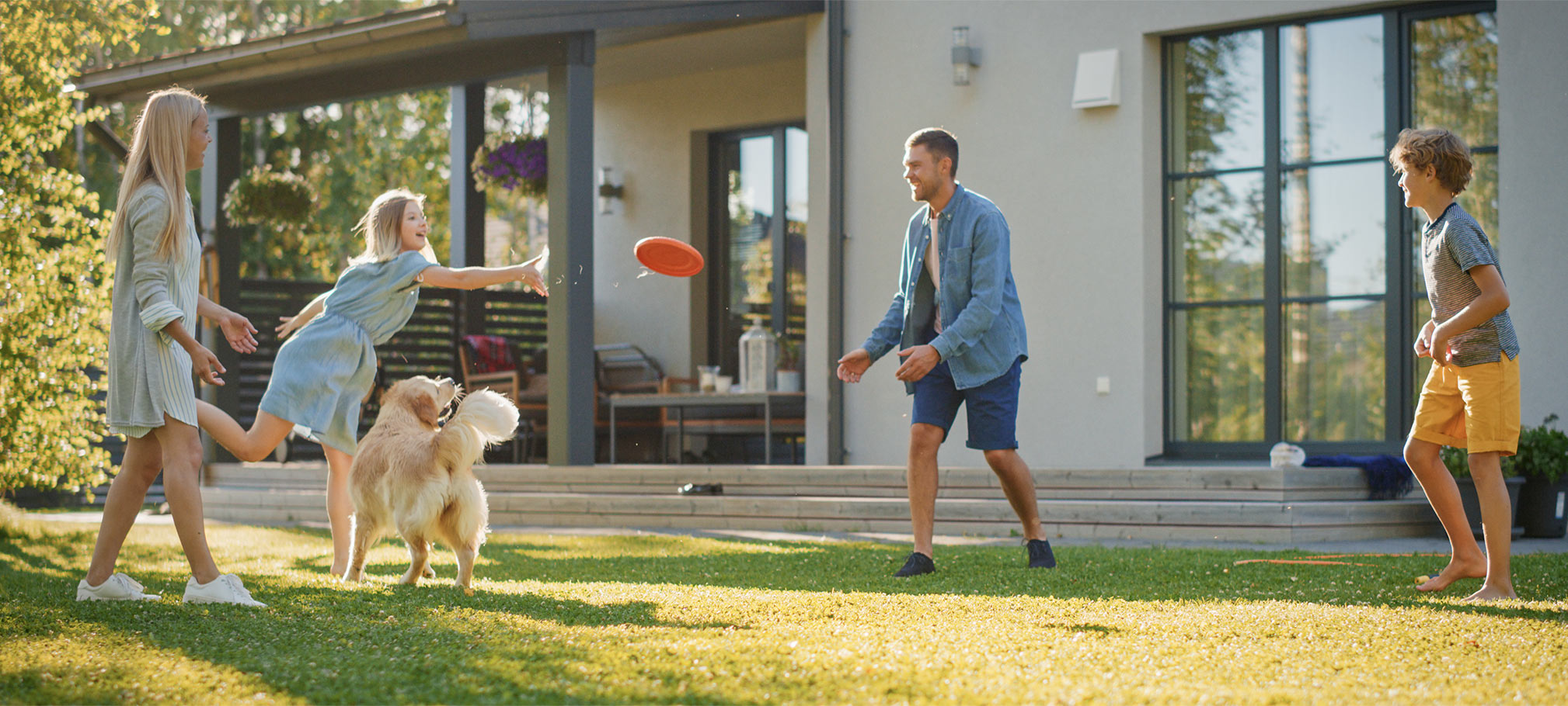 A family and their dog playing frisbee on a sunny lawn in their backyard.