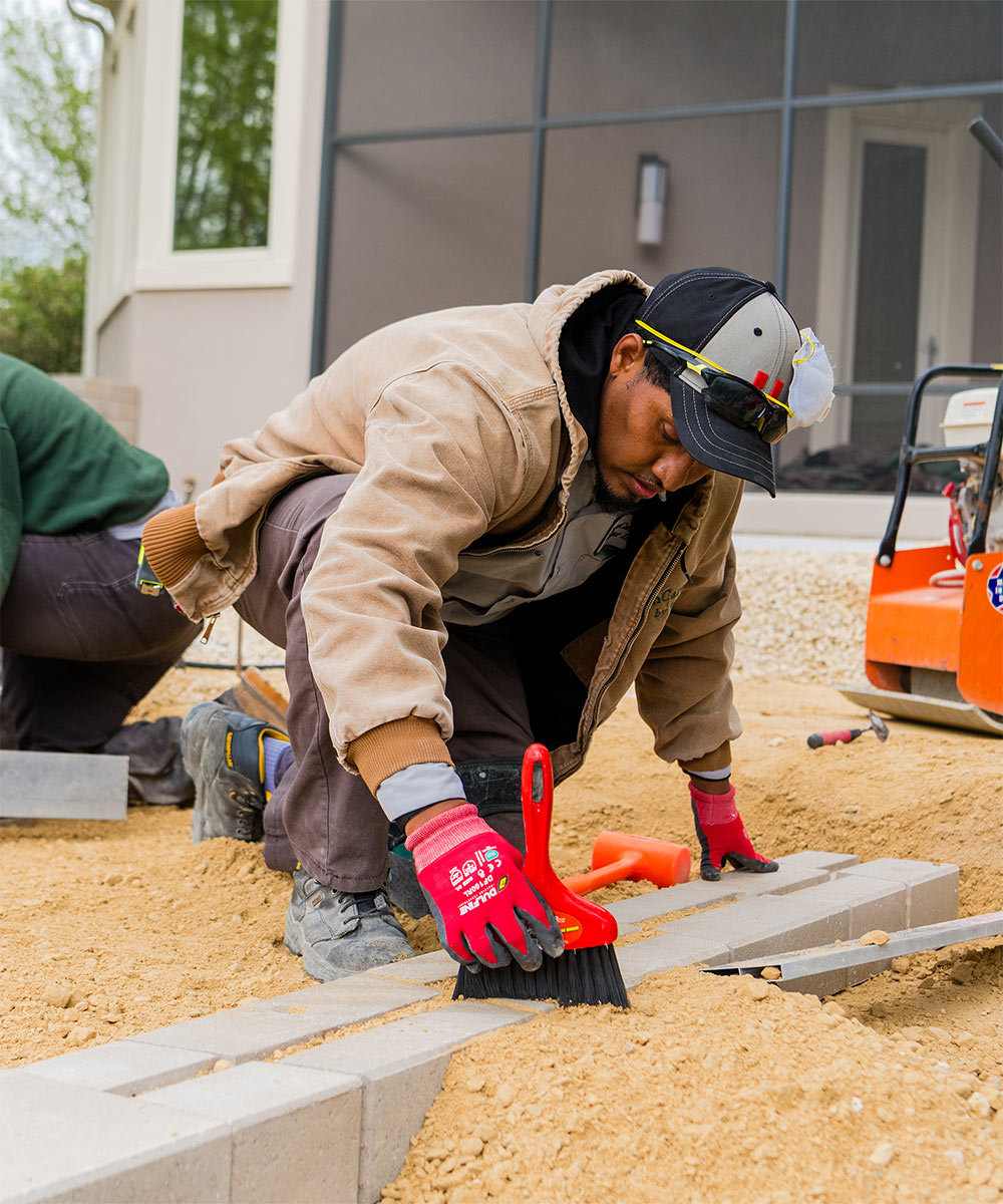 LawnCare by Walter hardscaping crew carefully laying retaining wall blocks and leveling paver stones.